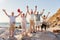 Portrait Of Senior Friends Standing On Rocks By Sea On Summer Group Vacation With Arms Outstretched
