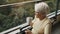 Portrait of senior gray haired woman with eyeglasses drinking cup of coffee in the wheelchair in front of the window