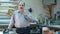 Portrait of a senior male business owner behind the counter of his frame workshop, standing and talking to a camera