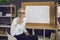 Portrait of a senior positive online math teacher sitting at a board with math formulas.