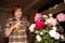 Portrait of senior smiling happy woman with dark hair wearing checkered shirt, spraying bouquet of pink, white roses.
