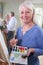 Portrait Of Senior Woman Attending Painting Class With Teacher          In Background