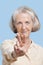 Portrait of senior woman in casuals gesturing peace sign against blue background