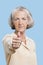 Portrait of senior woman in casuals gesturing thumbs up against blue background