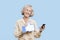 Portrait of senior woman with cell phone holding fake like button against blue background