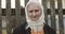 Portrait of a senior woman with deep wrinkles in a scarf on the background of an old fence.