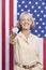 Portrait of senior woman holding election badge against American flag