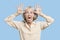 Portrait of senior woman making funny faces with hands on head against blue background