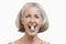 Portrait of senior woman with pill between her teeth against white background