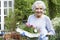 Portrait Of Senior Woman Planting Flowers In Garden