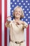 Portrait of senior woman pointing at election badge against American flag