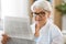 Portrait of senior woman reading newspaper at home