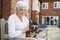 Portrait Of Senior Woman Sitting On Bench With Pet French Bulldog In Assisted Living Facility