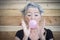 Portrait of senior woman in t shirt and bandanna showing balloon of bubble gum. Elderly woman having fun against wooden wall. Old