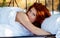 Portrait of an sensual, attractive, content, young, sexy, seductive redhead woman lying relaxed in bed, enjoying the nature in the