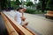 Portrait of a serene pensive woman with takeaway coffee in paper mug, sitting on wooden bench in the park