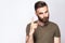 Portrait of serious bearded man with warning finger and dark green t shirt against light gray background.