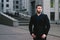 Portrait of a serious businessman in a dark suit and a beard against the backdrop of modern architecture.