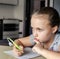 Portrait of serious elementary school girl writing a letter on a sheet of paper with pen in hand sitting at home table