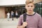 Portrait Of Serious Male High School Student Outside College Building With Other Teenage Students In Background