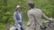 Portrait of serious man in helmet and formal suit sitting on scooter and listening to friend talking at front. Confident