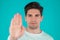Portrait of serious man showing rejecting gesture by stop palm hand sign. Guy isolated on blue background.