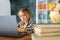 Portrait of serious pensive focused primary child school girl doing homework sitting at table with laptop and paper