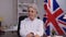 Portrait of serious professional mature businesswoman listening carefully sitting indoors in office with British flag at