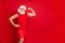 Portrait of serious santa claus in hat showing his triceps in training wearing sportswear cap isolated over red