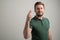 Portrait of serious stylish attractive man with thick beard, dressed in casual green t shirt showing fingers crossed