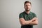 Portrait of serious stylish attractive man with thick beard, dressed in casual green t shirt standing with arms crossed