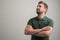 Portrait of serious stylish attractive man with thick beard, dressed in casual green t shirt standing with arms crossed