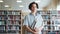 Portrait of serious teenage boy walking in school library with books alone