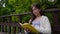 Portrait of serious teenage girl reading book and turning page leaning sitting on the bench in forest in spring