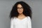 Portrait of serious woman with dark skin, Afro bushy hair, wears big transparent glasses and white soft sweater, looks directly at