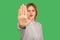 Portrait of serious young woman in classic striped blouse showing stop gesture to camera, warning with raised palm