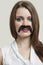 Portrait of serious young woman with fake mustache over gray background