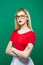 Portrait of Seriuos Girl Wearing Eyeglasses, Red Top and White Skirt on Green Background. Young Beautiful Woman with