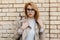 Portrait of a sexy cute young hipster woman in stylish glasses in a spring cloak in a white t-shirt near the vintage brick wall.