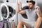 Portrait of sexy man with dirty clothes near washing machine. Handsome man sits in front of washing machine. Dirty