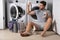 Portrait of sexy man with dirty clothes near washing machine. Handsome man sits in front of washing machine. Dirty