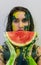 Portrait of a sexy, yellow, green painted woman, facepainting, holding a slice of fresh juicy watermelon in her hand