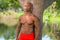 Portrait of a shirtless fitness model posing by a tree in the park. Image