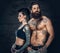 Portrait of shirtless, tattooed bearded male and brunette female with tattoo ink on her torso.