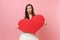 Portrait of shocked amazed bride woman in beautiful white wedding dress holding empty blank red heart isolated on pastel