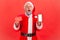 Portrait of shocked elderly man with gray beard wearing santa claus costume holding smart phone with
