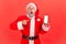 Portrait of shocked elderly man with gray beard wearing santa claus costume pointing at blank