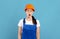 Portrait Of Shocked Handywoman In Hardhat And Coveralls Standing Over Blue Background