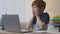 Portrait of shocked little redhead boy looking at laptop with amazed expression, touching his cheeks in amazement