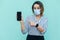 Portrait of shocked middle aged woman with surgical medical mask standing and showing mobile smart phone display with big eyes